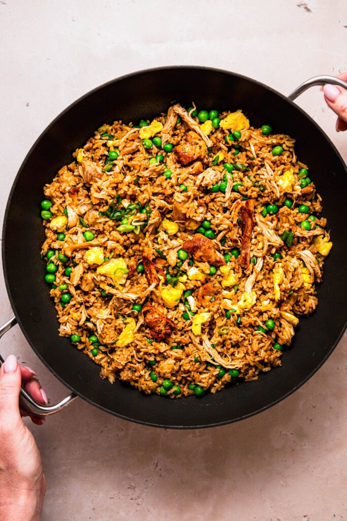 Hands holding wok full of finished rotisserie chicken fried rice.