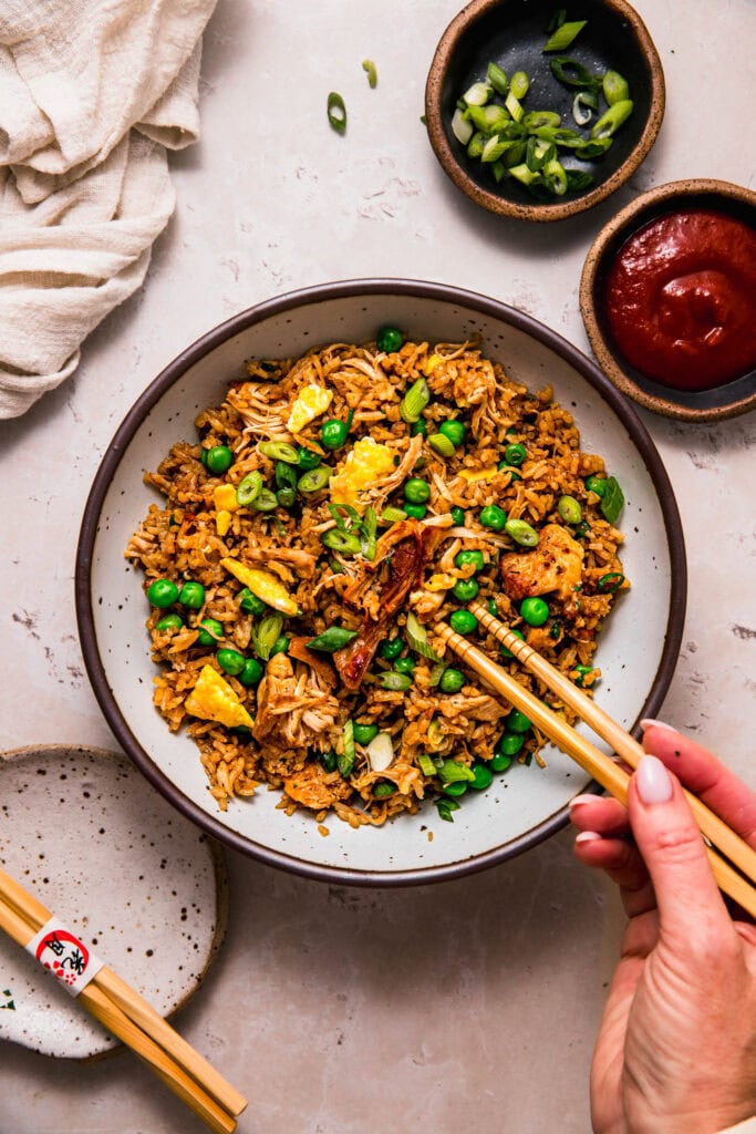 Hands holding chopsticks dipping into bowl of rotisserie chicken fried rice.