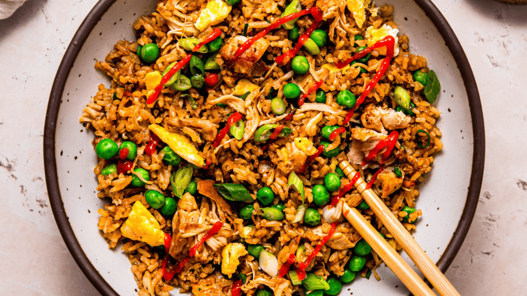 Bowl of rotisserie chicken fried rice topped with sriracha sauce.