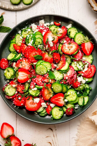 Strawberry cucumber salad served on a green plate with fresh strawberries and cucumber slices nearby.