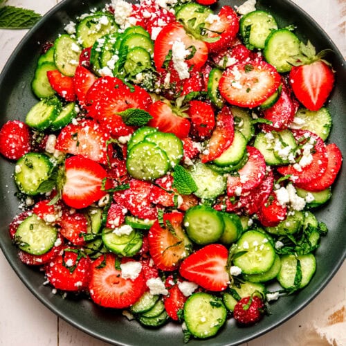 Strawberry cucumber salad served on a green plate with fresh strawberries and cucumber slices nearby.