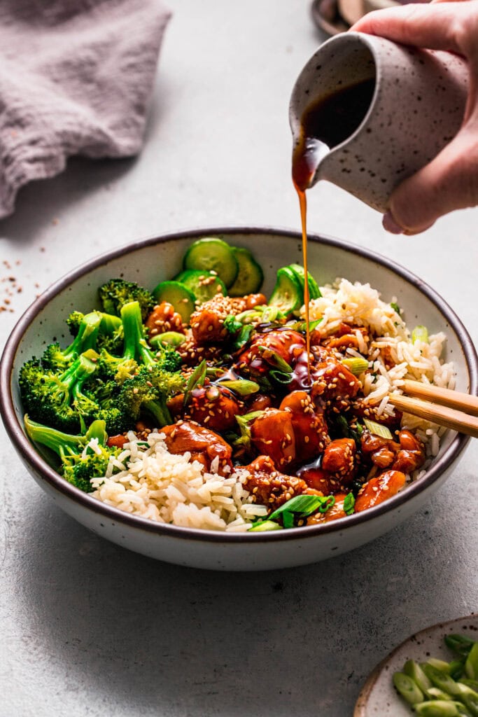Side view of teriyaki chicken rice bowl being drizzled with teriyaki sauce.