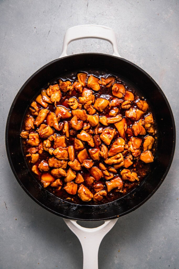 Chicken pieces in skillet tossed with teriyaki sauce.
