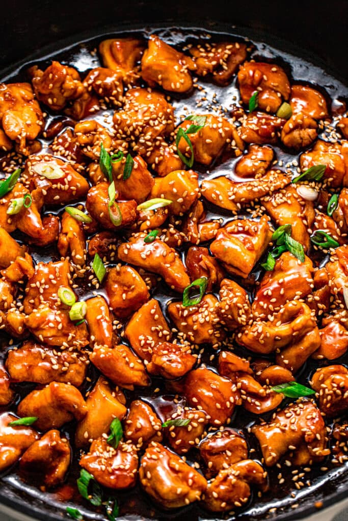Overhead close up of Chicken pieces in skillet tossed with teriyaki sauce sprinkled with green onions and sesame seeds.