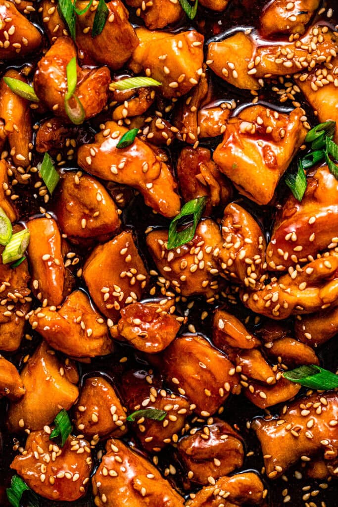 Overhead close up of Chicken pieces in skillet tossed with teriyaki sauce sprinkled with green onions and sesame seeds.