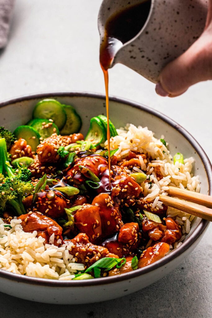 Teriyaki sauce being drizzled onto bowl of chicken and broccoli.