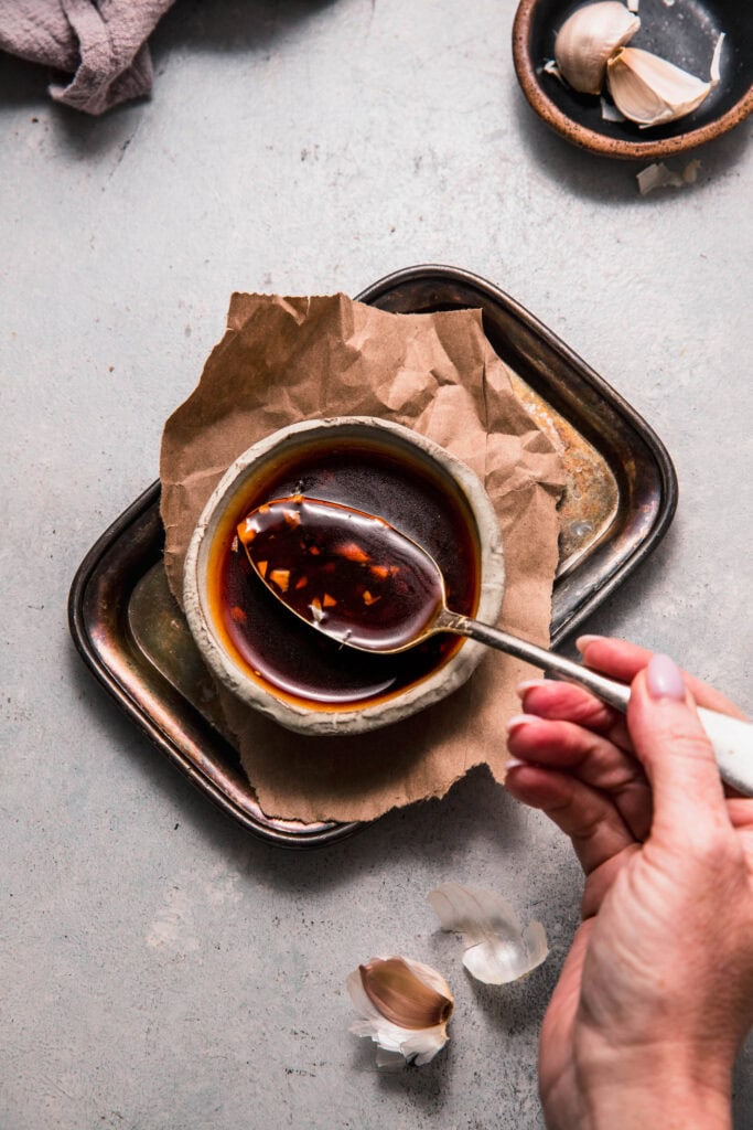 Hand dipping spoon into bowl of teriyaki sauce.