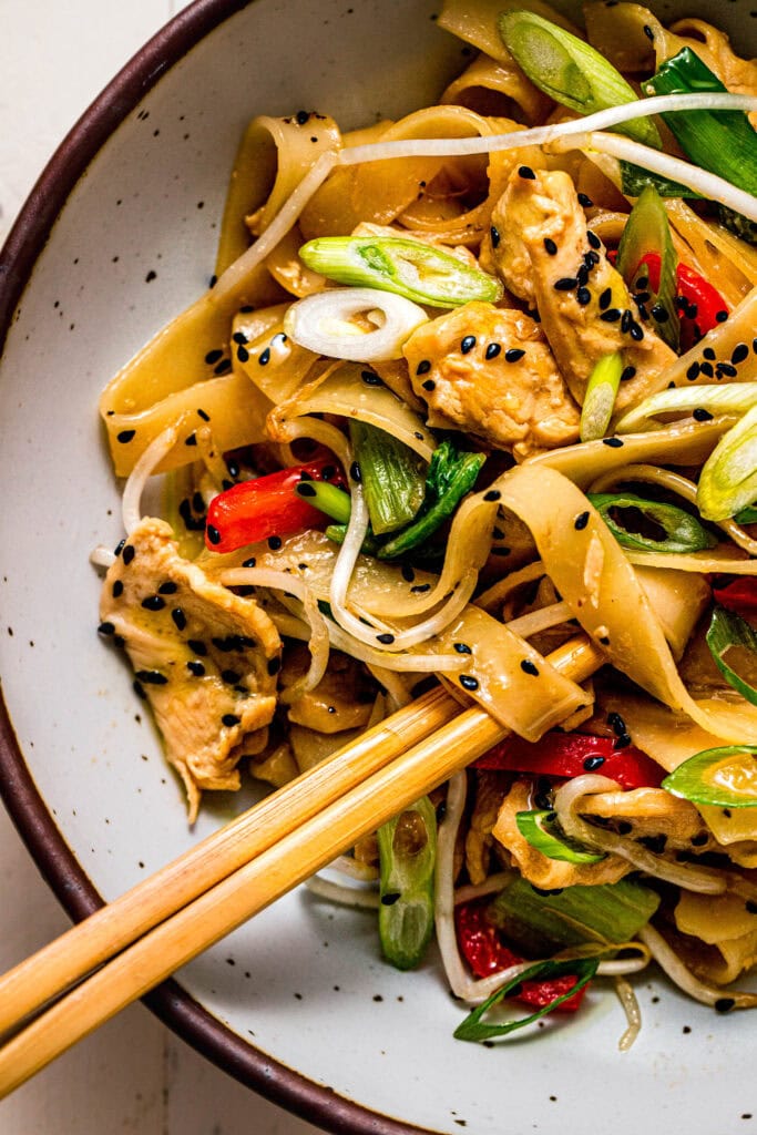 Overhead close up of chicken chow fun in serving bowl with chopsticks.