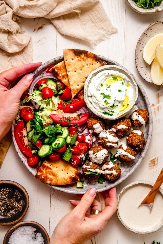 Hands holding plate of chicken shawarma meatballs.