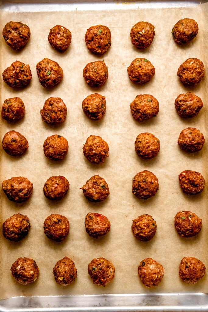 Formed cooked meatballs on baking sheet.