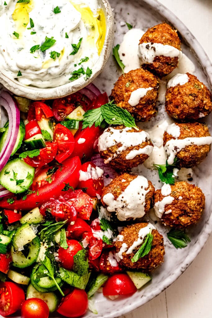Overhead close up of finished chicken shawarma meatballs on plate with bowl of tzatziki sauce.