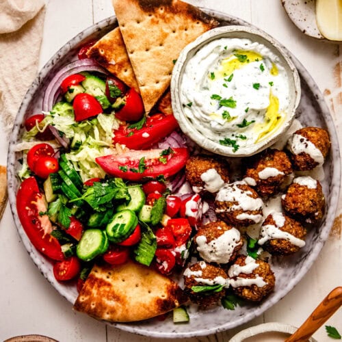 Finished chicken shawarma meatballs on plate with tzatziki sauce and pieces of pita.
