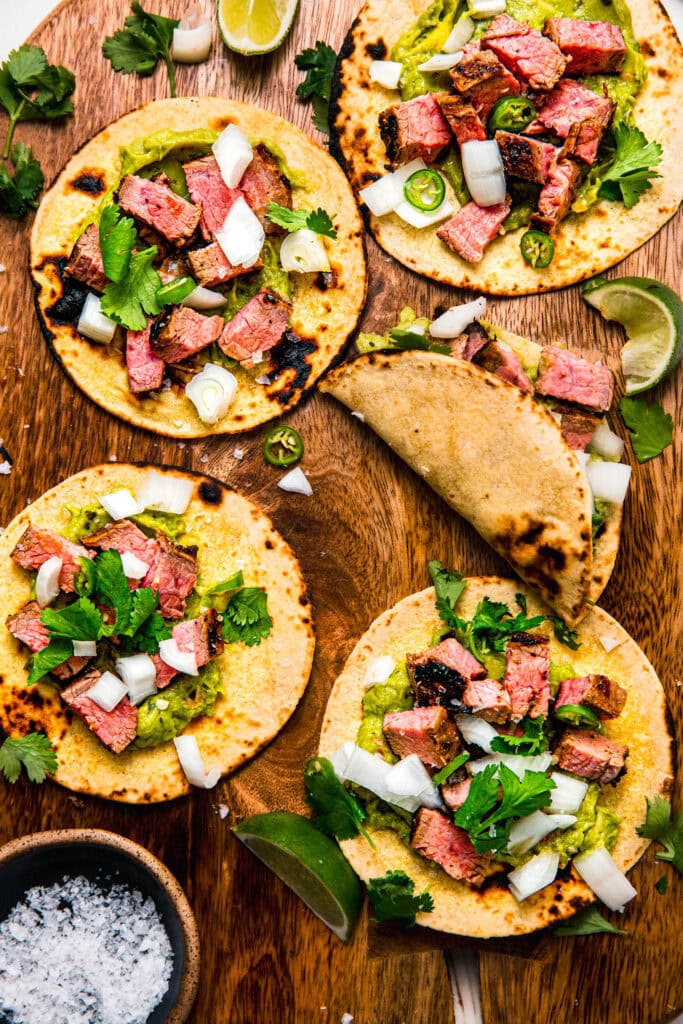 Assembled grilled carne asada tacos on serving platter topped with cilantro and onions.