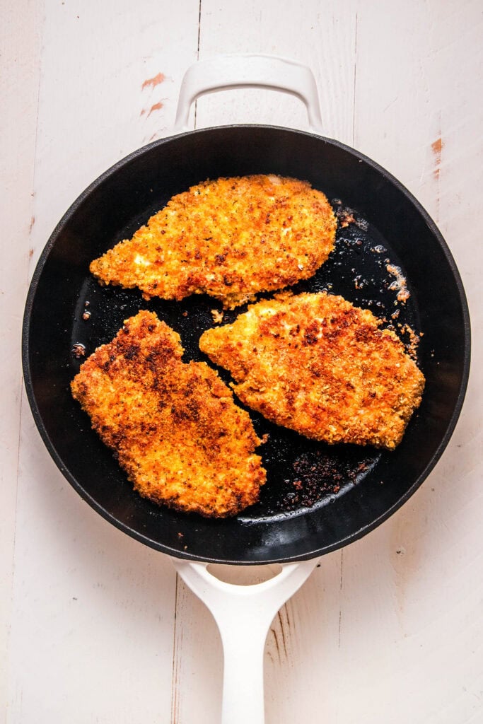 Breaded chicken cutlets browning in skillet.