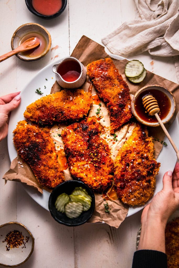 Hands holding platter of hot honey chicken.