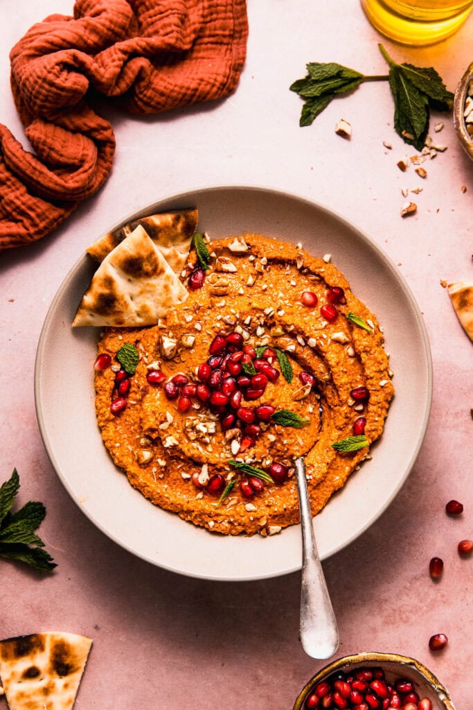 Muhammara dip in serving bowl sprinkled with pomegranate seeds, parsley and chopped nuts.