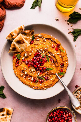 Overhead view of roasted red pepper muhammara dip with pomegranate seeds, fresh herbs, and chopped nuts.