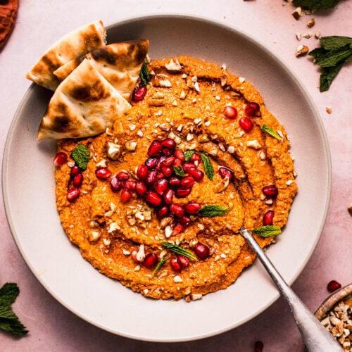Overhead view of roasted red pepper muhammara dip with pomegranate seeds, fresh herbs, and chopped nuts.