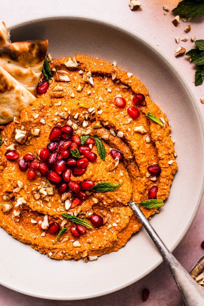 Close-up of homemade muhammara dip finished with pomegranate seeds, parsley, and chopped walnuts.
