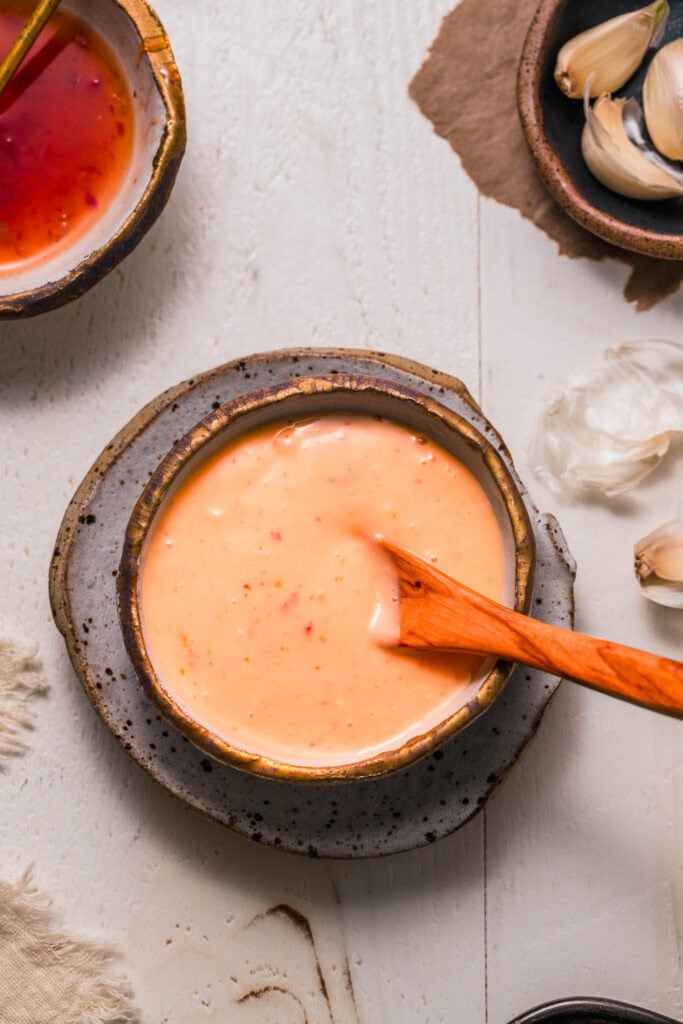 Spoon dipping into small bowl of sweet chili aioli.