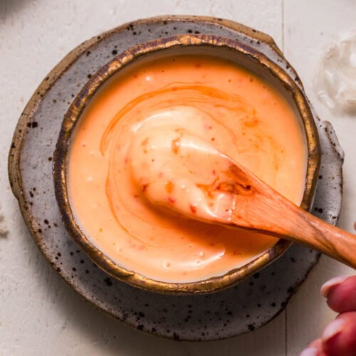 Hand dipping spoon into bowl of sweet chili aioli sauce.