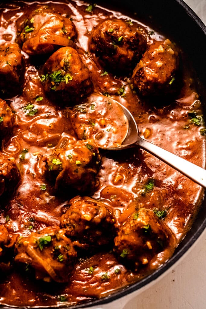 Side view of salisbury steak meatballs in skillet with spoon.