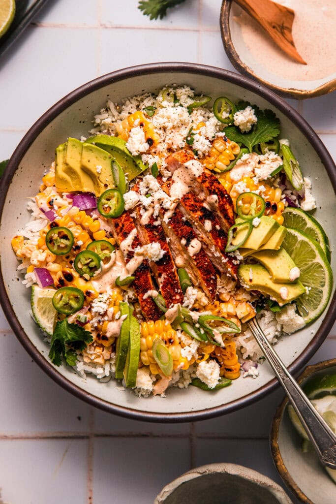 Street corn chicken and rice bowl topped with seasoned chicken, charred corn, and a creamy smoky dressing.