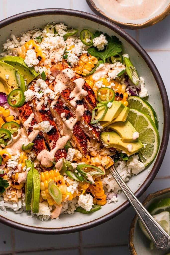 Close-up of a street corn chicken bowl with seasoned chicken, fluffy rice, smoky corn, and a rich, creamy topping.