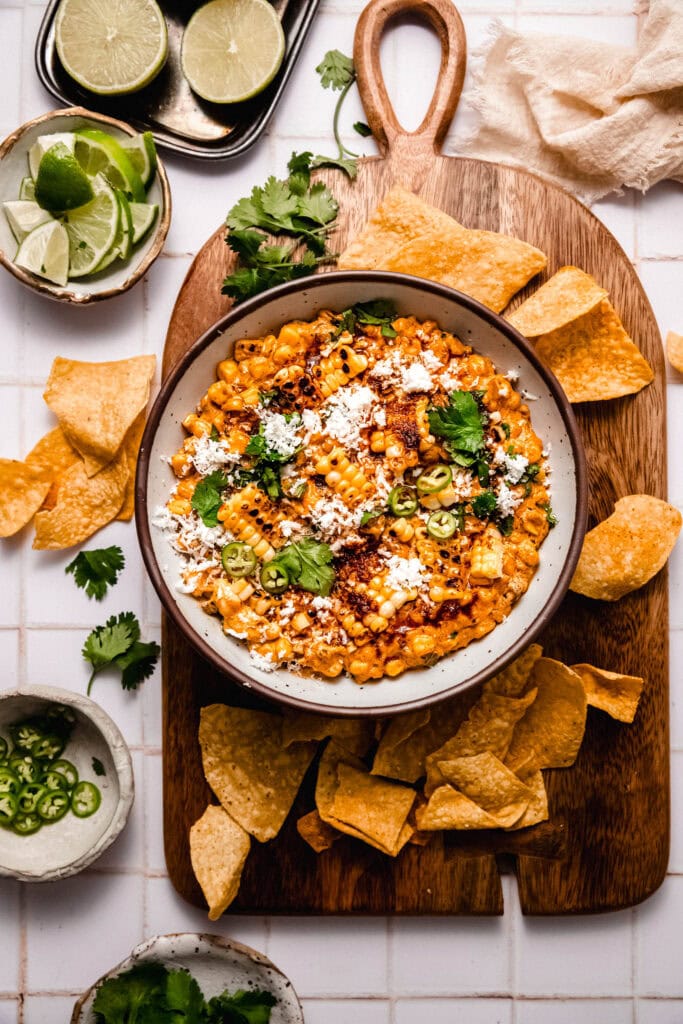 Bowl of prepared street corn dip on serving tray surrounded by tortilla chips.