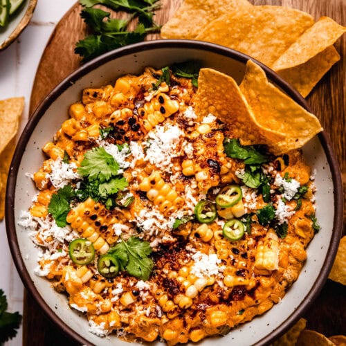 Overhead shot of bowl of elote dip with chips dipped into it.