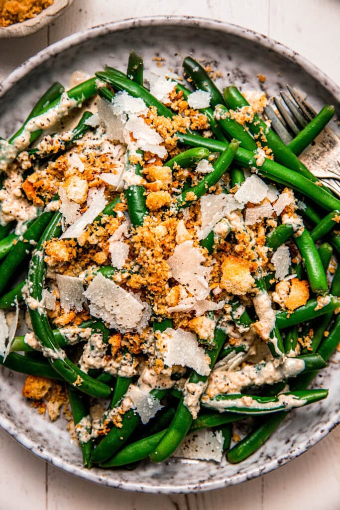 Overhead close up of caesar green beans drizzled with dressing and topped with crispy breadcrumbs.