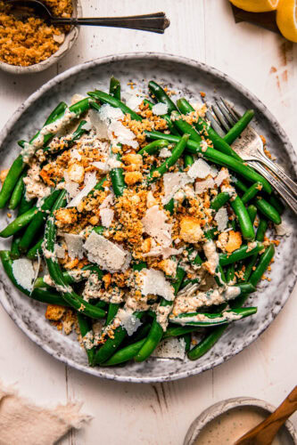 Prepared caesar green bean salad on grey plate topped with shaved parmesan and crispy breadcrumbs.