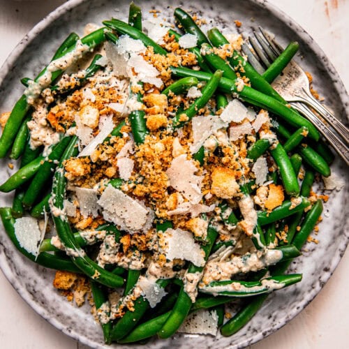 Prepared caesar green bean salad on grey plate topped with shaved parmesan and crispy breadcrumbs.