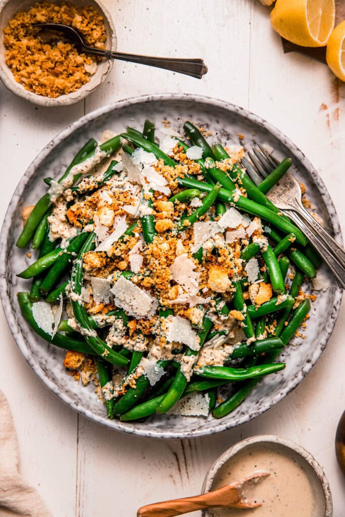 Prepared caesar green bean salad on grey plate topped with shaved parmesan and crispy breadcrumbs.
