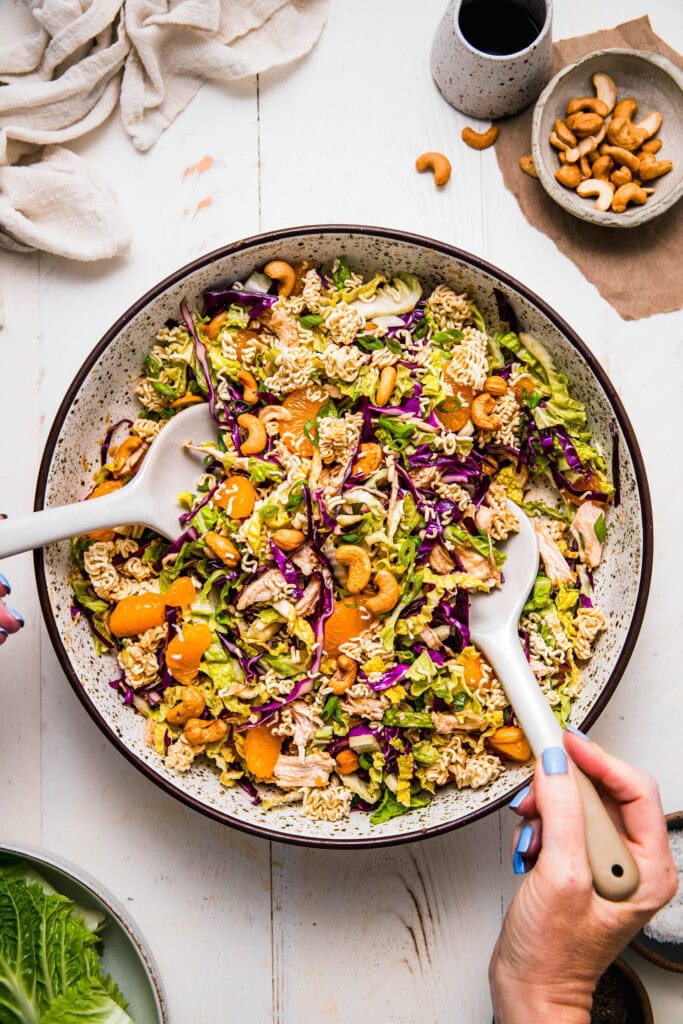 Prepared chinese chicken salad in serving bowl with serving spoons.