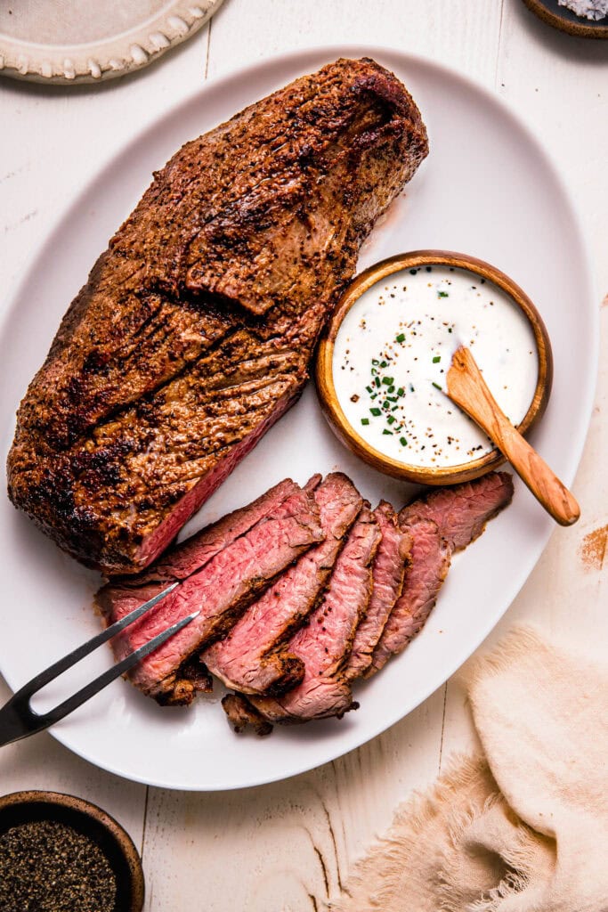 PLATE OF CARVED PRIME RIB NEXT TO SMALL BOWL OF CREAMY HORSERADISH.