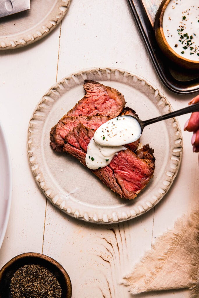 CREAMY HORSERADISH BEING DRIZZLED ONTO PLATE OF PRIME RIB.