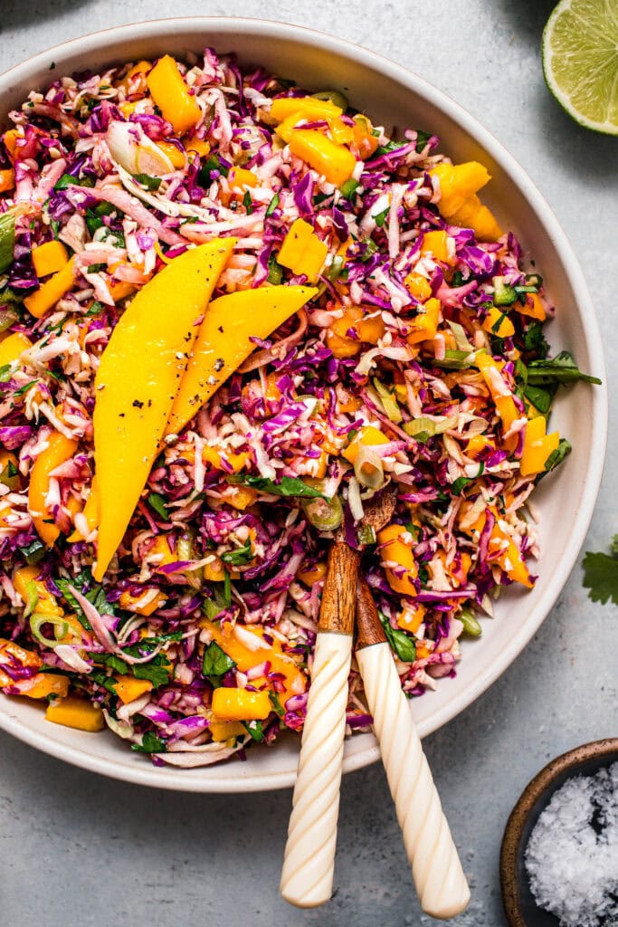Overhead close up of prepared mango slaw in bowl with serving tongs.