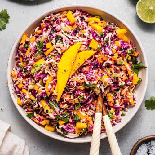 Mango coleslaw served in white bowl next to bowl of sliced mango.