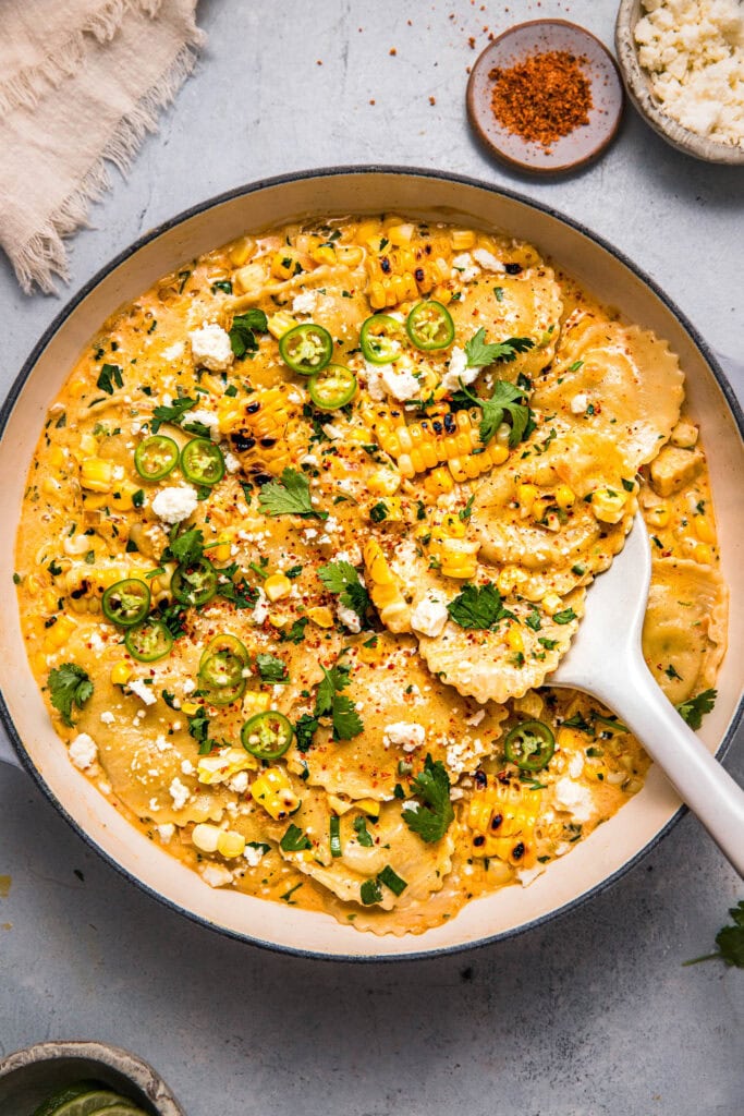 Street corn ravioli in skillet with serving spoon.