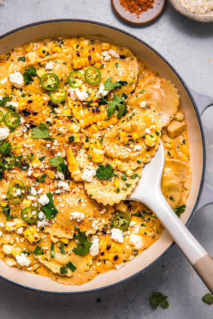 Street corn ravioli in skillet with serving spoon.