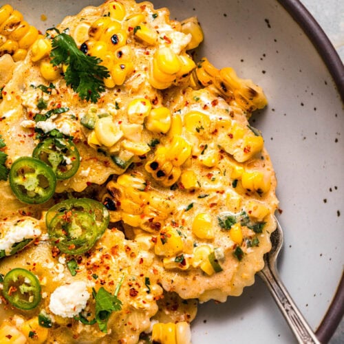 Overhead close up of bowl of street corn ravioli topped with sliced jalapenos and sprinkled with tajin.