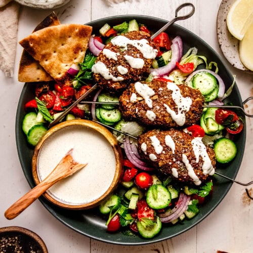 Prepared turkey kofta on plate drizzled with tahini sauce and served with cucumber tomato salad.