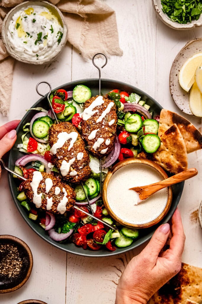 Hands holding platter of finished turkey kofta. 