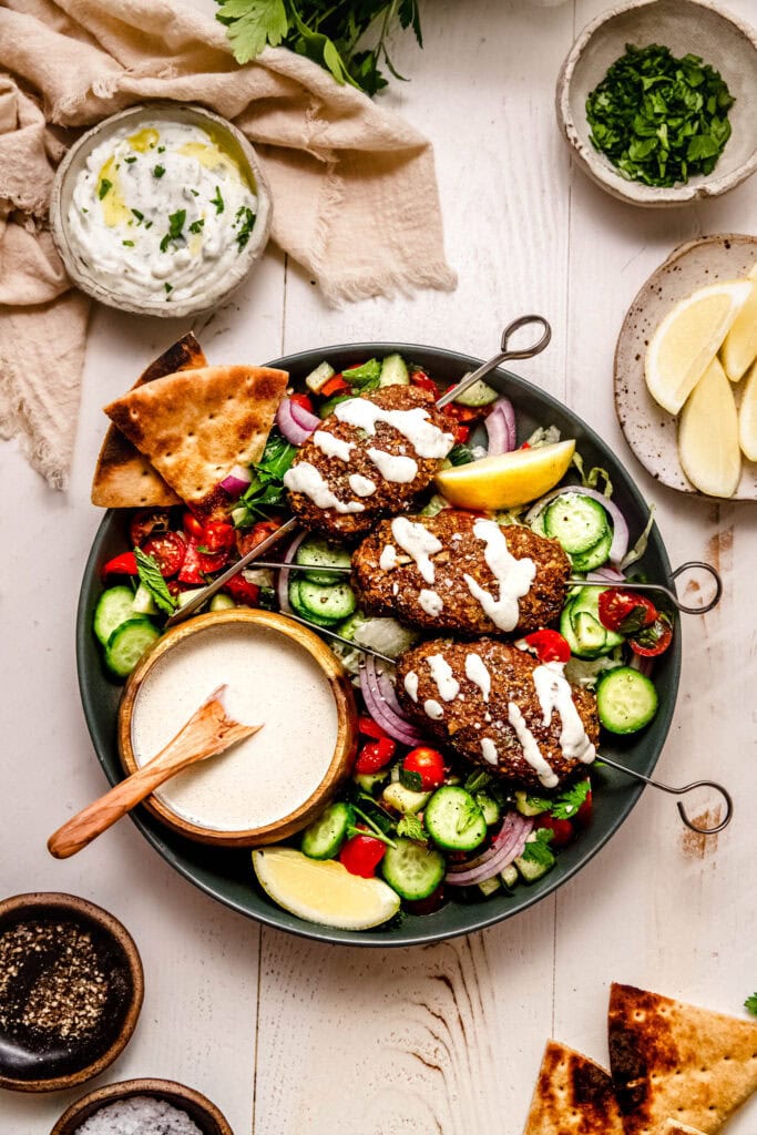 Middle Eastern-inspired turkey kofta on a plate with a tahini drizzle and colorful cucumber tomato salad.