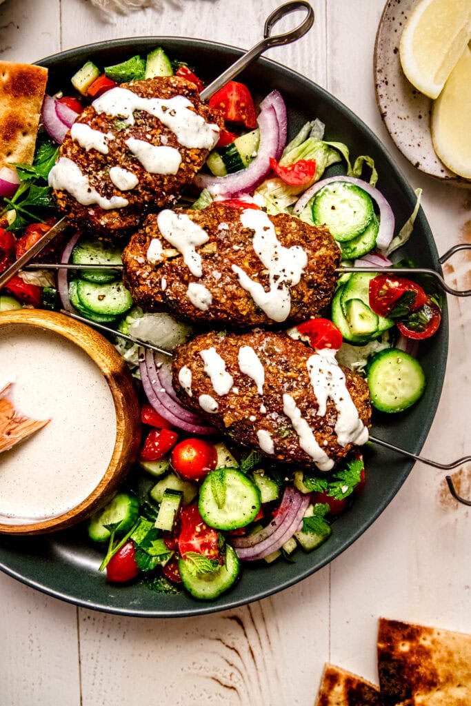 Turkey kofta served on a plate, drizzled with creamy tahini sauce and paired with cucumber tomato salad.