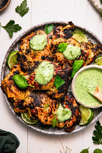 Overhead shot of plate of chicken thighs topped with green goddess sauce.