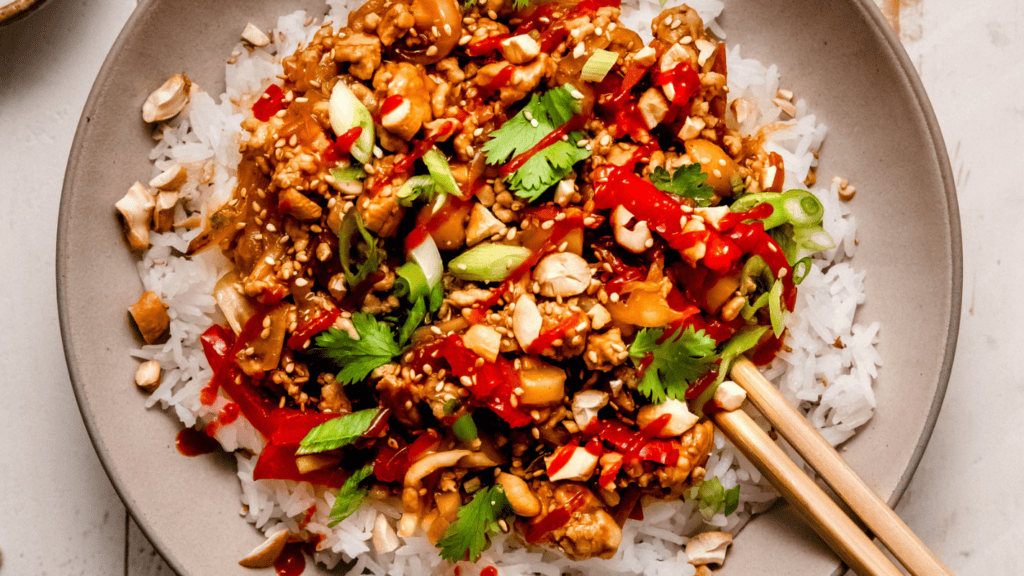 Horizontal image of ground pork stir fry in serving bowl with a bed of rice.
