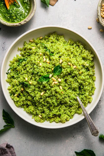 Overhead shot of bowl of pesto quinoa topped with pine nuts and basil.