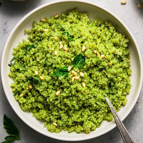 Overhead shot of bowl of pesto quinoa topped with pine nuts and basil.